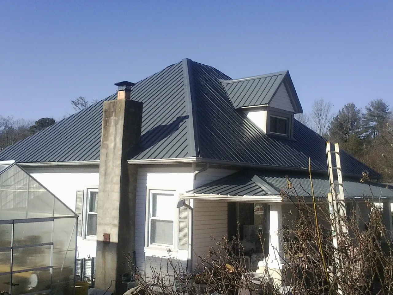 Dark blue standing seam metal roof on a white farmhouse with dormer — Slate & Tile Roof Repair by Roofing Brothers in Barnstable