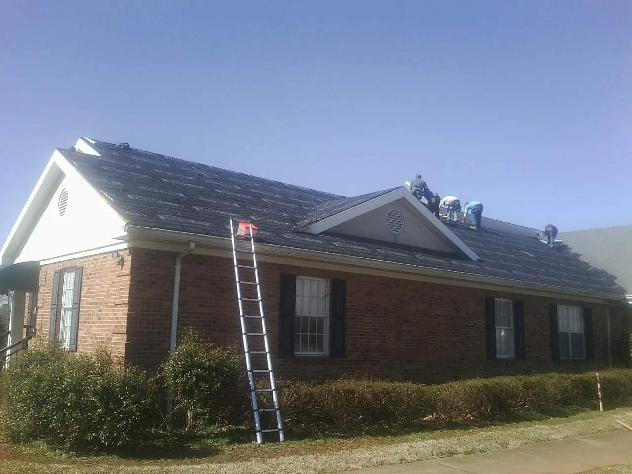 Crew tearing shingles off a brick ranch roof with a ladder set — Emergency Roof Repair work by our crew in Barnstable