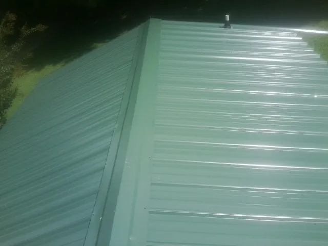 New green metal panels meeting at the ridge of a roof — Flat Roof Repair work by our crew in Barnstable