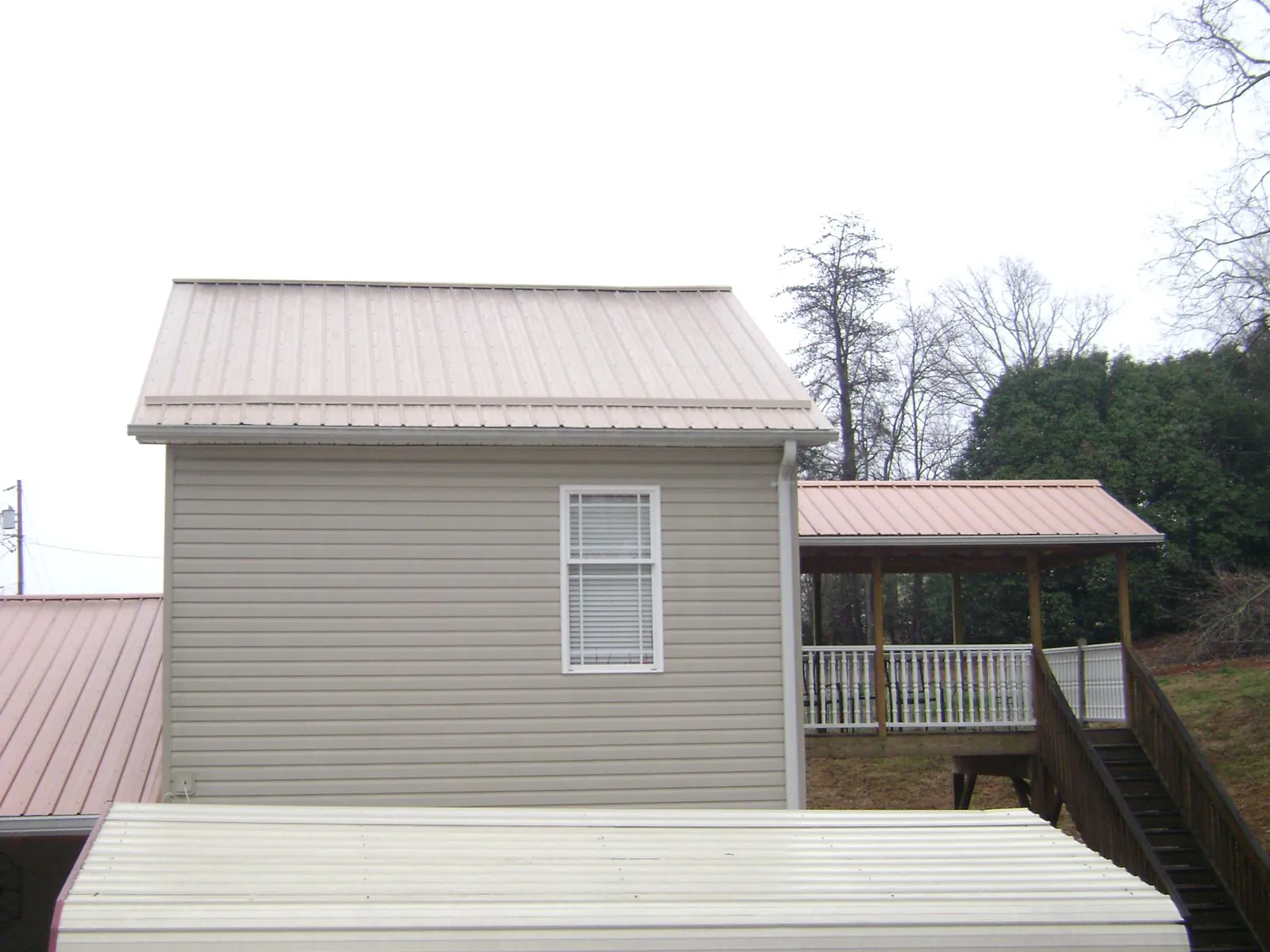 Tan metal roofs on a two story addition and attached porch, from a Roof Replacement job in Barnstable