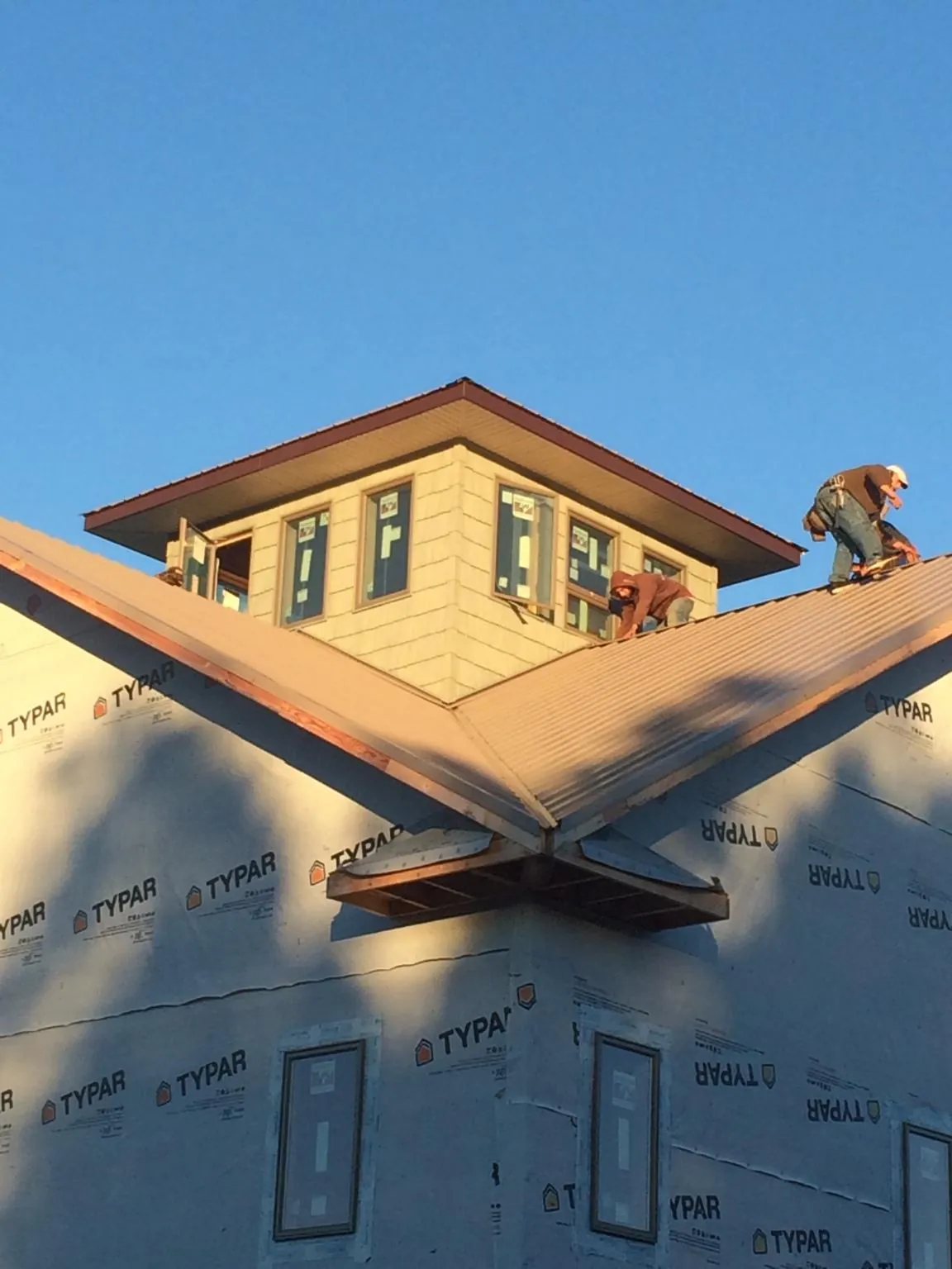 Roofers working around a rooftop cupola on a new metal roof at sunset — Roof Waterproofing in Barnstable by Roofing Brothers
